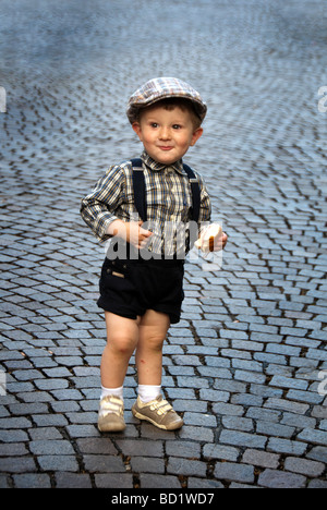 Little Boy circa 2 anni di indossare abbigliamento retrò ad una festa tradizionale di mangiare mirenda (snack) su di una strada asfaltata Foto Stock