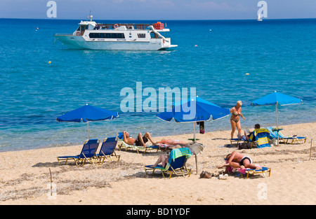 I turisti rilassandovi sulle sdraio sotto gli ombrelloni sulla spiaggia sabbiosa di Skala sull'isola greca di Cefalonia Grecia GR Foto Stock