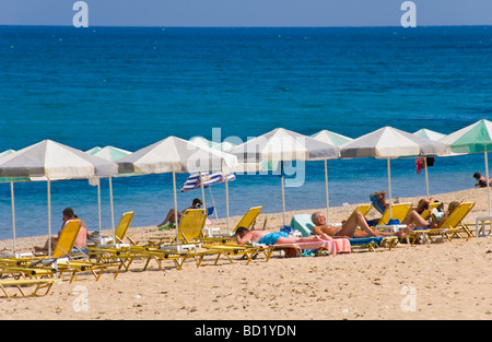 I turisti rilassandovi sulle sdraio sotto gli ombrelloni sulla spiaggia sabbiosa di Skala sull'isola greca di Cefalonia Grecia GR Foto Stock