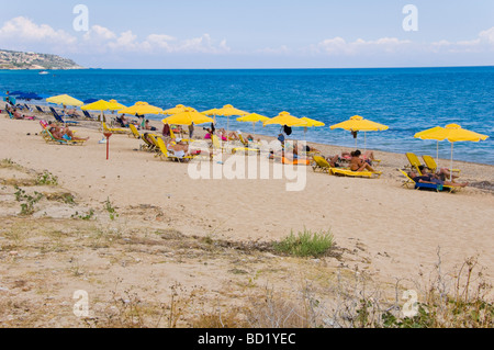 I turisti rilassandovi sulle sdraio sotto gli ombrelloni sulla spiaggia sabbiosa di Skala sull'isola greca di Cefalonia Grecia GR Foto Stock