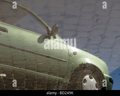 Uno verde auto parcheggiata la riflessione sulla strada allagata Foto Stock