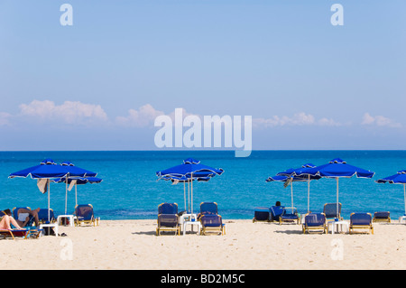 I turisti rilassandovi sulle sdraio sotto gli ombrelloni sulla spiaggia sabbiosa di Skala sull'isola greca di Cefalonia Grecia GR Foto Stock