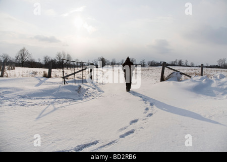 Donna che cammina attraverso i campi innevati Foto Stock