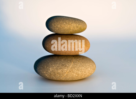 Ancora vita colpo di tre spiaggia ciottoli equilibrato in una pila di pietra contro uno sfondo bianco con illuminazione artificiale Foto Stock