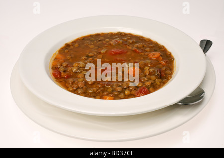 Ciotola di zuppa di lenticchie con pomodori e carote con cucchiaio su sfondo bianco. Foto Stock