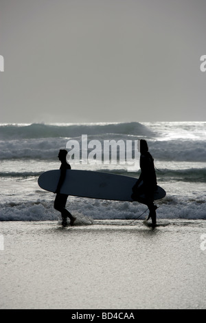 Area del Watergate Bay, Inghilterra. Stagliano vista di due surfisti che porta una tavola da surf su un mare tempestoso giorno. Foto Stock