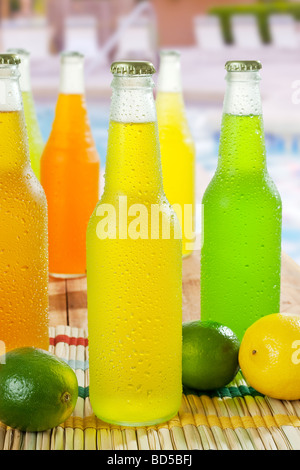 Immagine ravvicinata di bottiglie fredde con bevande tropicali su un tavolo intorno alla piscina Foto Stock