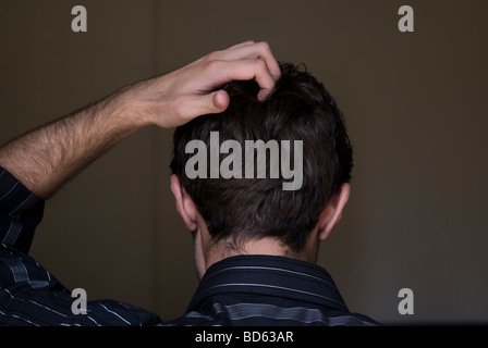 Vista posteriore di un giovane uomo di graffiare la sua testa Foto Stock