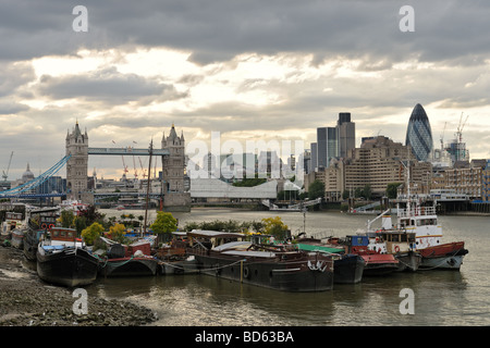 Case galleggianti ormeggiate sulla riva sud del fiume Tamigi a Londra con il Tower Bridge e la drammatica skiy in background Foto Stock