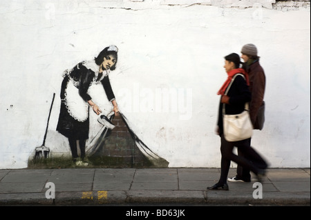 Due pedoni a piedi passato Banksy pulito le strade artwork su un muro di Chalk Farm Road, London NW1, Dicembre 2007 Foto Stock