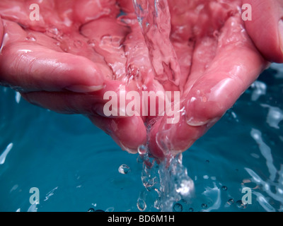 Le donne le mani in acqua che scorre su sfondo blu Foto Stock