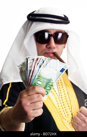 Uomo che indossa un costume di Sheikh, fumare un sigaro e tenendo un fan di banconote in euro in sua mano Foto Stock