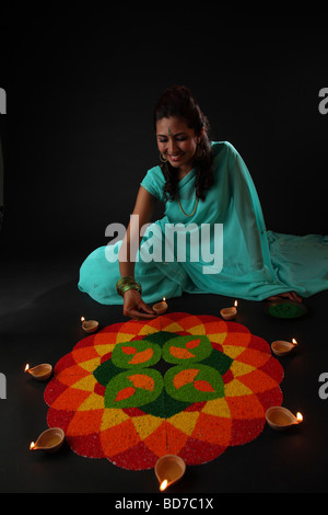 Angolo di alta vista di una giovane donna di decorare rangoli con lampade a olio Foto Stock