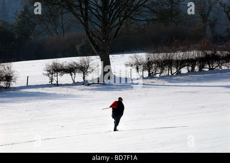 Un agricoltore a piedi attraverso una coperta di neve nel campo di Kington, Herefordshire Foto Stock