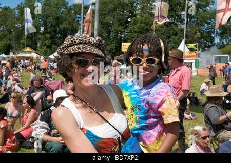 Un sorridenti mamma indossando occhiali da sole mentre tiene il suo bambino davanti a una folla di persone al festival Womad Foto Stock