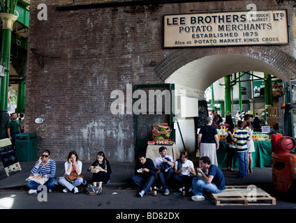 Persone sedersi e mangiare sul pavimento vicino a Lee fratelli, Borough Market, Londra Foto Stock