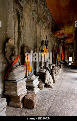 Una fila di rotture di statue di Buddha con arancione vesti all'interno di un cortile di Angkor Wat Foto Stock