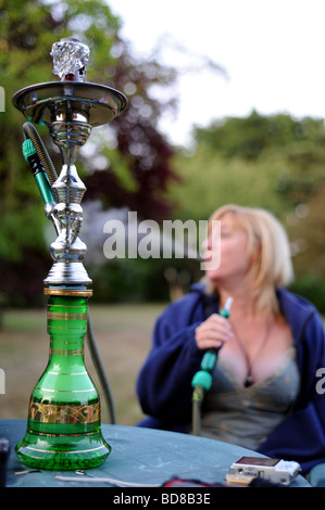 Una donna che fuma da un bagno turco hookah al di fuori della tubazione in una serata estiva Foto Stock