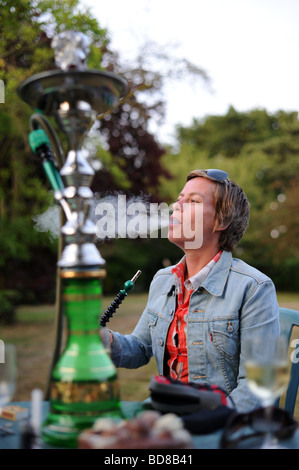 Una donna che fuma da un bagno turco hookah al di fuori della tubazione in una serata estiva Foto Stock