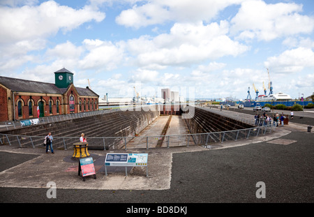 Thompson Dock, la graving dock del RMS Titanic e la Pumphouse, Belfast, Irlanda del Nord, con turisti, alcune su un banco. Foto Stock