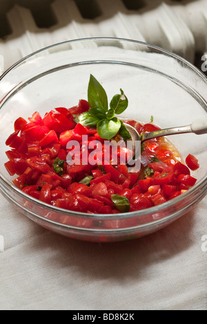 Ciotola di fresco tritato pomodori italiane con un rametto di basilico fresco per il periodo estivo sugo per la pasta Foto Stock