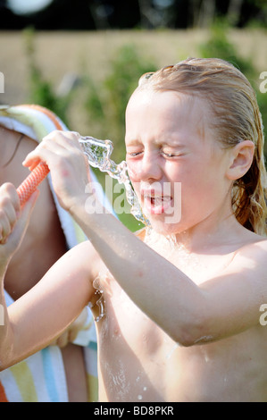 Fotografia di una ragazza di lavaggio e raffreddamento con tubo flessibile di acqua su un giorno di estate nel giardino Inglese UK Foto Stock