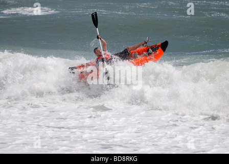 Un uomo su un Blow up canoa scuffiata in surf ruvida Foto Stock