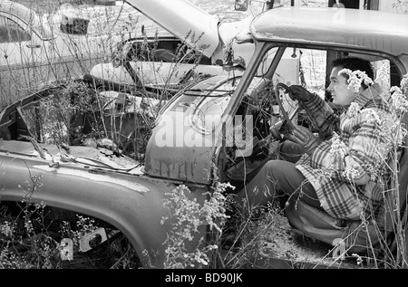 Un uomo di mezza età che finge di guidare un auto o camion in a junkyard nel periodo invernale Foto Stock