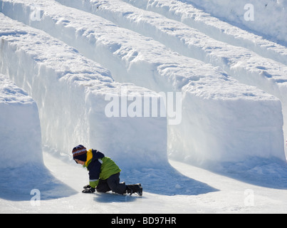 Dopo la diapositiva. Un giovane ragazzo cerca di alzarsi in piedi sul ghiaccio scivoloso appena al di sotto di una neve e ghiaccio slitta a Winterlude. Foto Stock