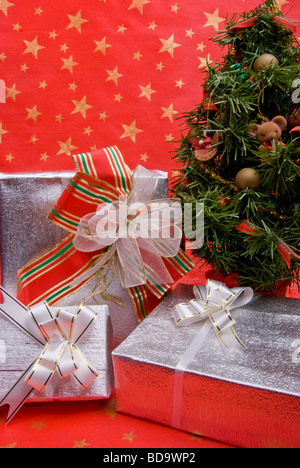 Tre pacchetti regalo vicino all'albero di Natale su uno sfondo di colore rosso decorato con stelle dorate Foto Stock