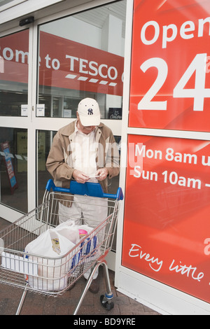 Il vecchio uomo nel controllo della sua ricezione al di fuori del supermercato Tesco Blackpool Lancashire Inghilterra Foto Stock