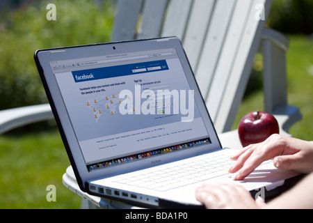 Donna con notebook che mostra il social networking Facebook schermata splash page Foto Stock