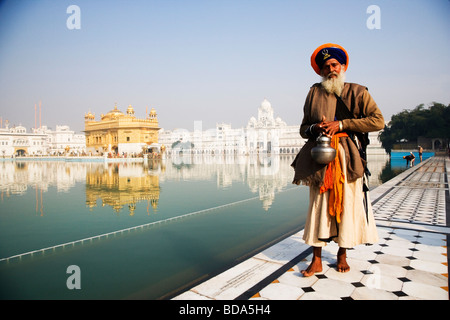 Sadhu camminare nei pressi di un laghetto con un tempio in background, Tempio Dorato, Amritsar Punjab, India Foto Stock