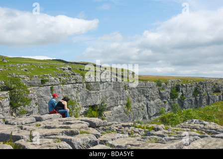 Giovane seduto sul pavimento di calcare sulla sommità di Malham Cove, Yorkshire Dales National Park, North Yorkshire, Inghilterra, Regno Unito Foto Stock