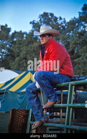 Giovani cowboy si siede sul recinto affacciato su rodeo arena Foto Stock