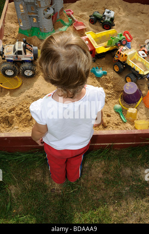 Bambino ragazza nella buca di sabbia giocare con spade e giocattoli auto automobili parco giochi del veicolo 2 3 4 anni Foto Stock