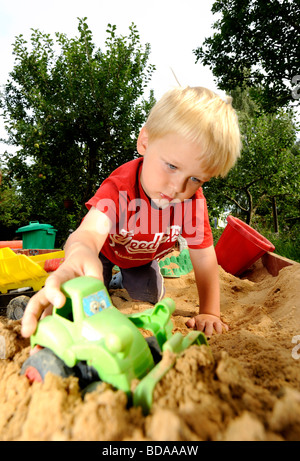 Baby boy ragazzi nella buca di sabbia giocare con spade e giocattoli auto automobili parco giochi del veicolo 2 3 4 anni Foto Stock