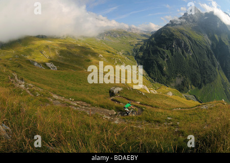 Un mountain biker cavalca un ripido sentiero alto sopra una valle in Les Arcs nelle Alpi francesi. Foto Stock