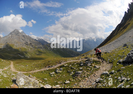 Un mountain biker cavalca un sentiero roccioso alto sopra una valle in Les Arcs, nelle Alpi francesi Foto Stock