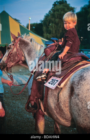 Giovani 4, 5, 6 anno vecchio ragazzo si siede in rodeo sella di cavallo alla fiera di paese Foto Stock