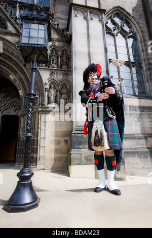 Un suonatore di cornamusa scozzese in pieno uniforme del vestito svolge la sua cornamusa fuori l'ingresso alla Cattedrale di St. Giles in Edinburgh Royal Mile. Foto Stock