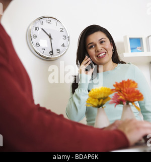 Metà vista in sezione di un uomo che utilizza un computer portatile con una metà donna adulta a parlare su un telefono mobile in background Foto Stock