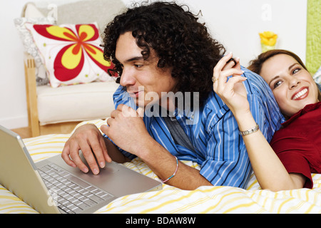 Giovane uomo che utilizza un computer portatile con una giovane donna appoggiata sulla sua schiena e sorridente Foto Stock
