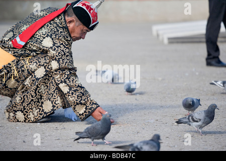 Il mongolo uomo indossando il costume tradizionale nutre gli uccelli, ad Ulaan Baatar, Mongolia Foto Stock