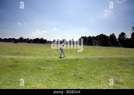 A WOMAN WALKS ALONE ACROSS A FIELD Between The historic village of Dedham and Flatford in Essex England Constable country Foto Stock