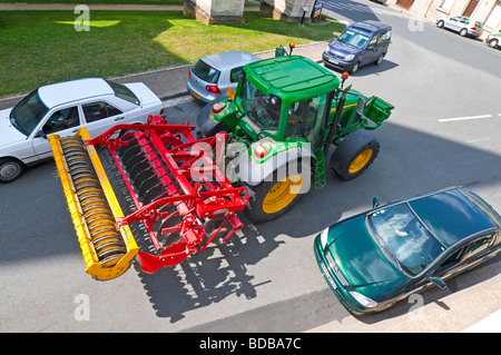 Trattore John Deere & Terradisc harrow negoziando automobili parcheggiate in città street - Indre-et-Loire, Francia. Foto Stock