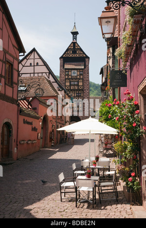 Pavement caffè Dolder Tower cancello e vecchi edifici su stretto Strada acciottolata nella pittoresca città medievale di Riquewihr Alsazia Francia Foto Stock