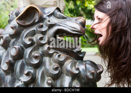 Ritratto di una giovane donna alla ricerca di una scultura di metallo di un leone in Sydney's Botanic Gardens, Australia Foto Stock