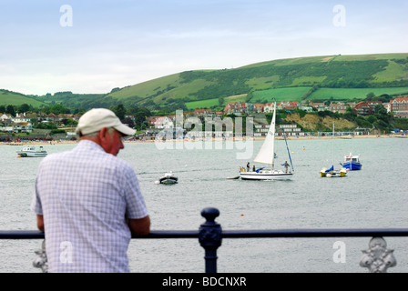 Swanage Bay con figura maschile in primo piano appoggiato sul molo di ringhiere Foto Stock