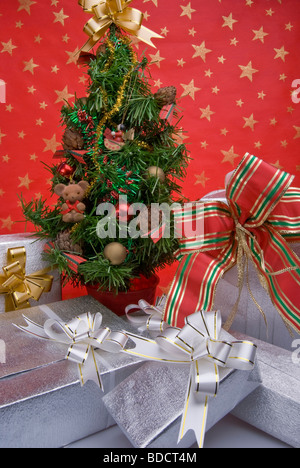 Cinque pacchetti regalo sotto un piccolo albero di Natale su uno sfondo di colore rosso decorato con stelle dorate Foto Stock